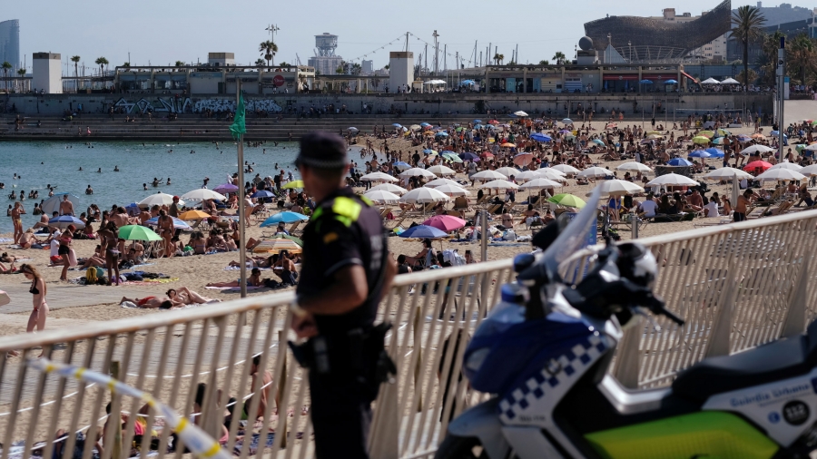 A police officer looks on as people enjoy the sunny weather on the beach, as Spain officially reopens the borders amid the coronavirus outbreak, in Barcelona, Spain, June 21, 2020. A police officer is shown in the nearground in soft focus with hundreds of beachgoers line the coast with umbrellas.