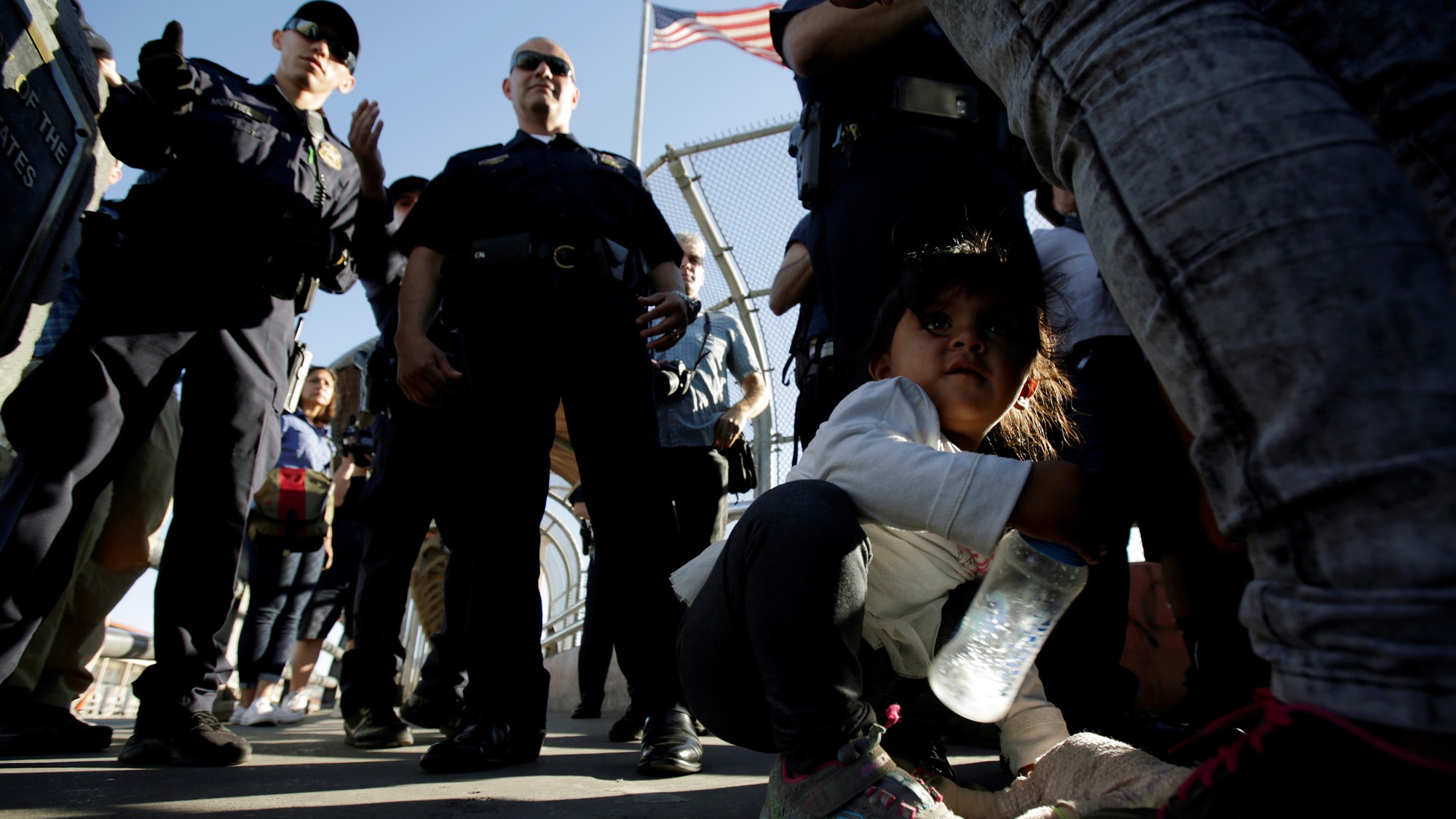 Migrant families from Mexico listen to officers of the US Customs and Border Protection before entering the United States to apply for asylum at Paso del Norte international border crossing bridge in Ciudad Juarez, Mexico, June 20, 2018. A you migrant girl crouches next to her family as they listen to officers of the US Customs and Border Protection before entering the United States to apply for asylum.
