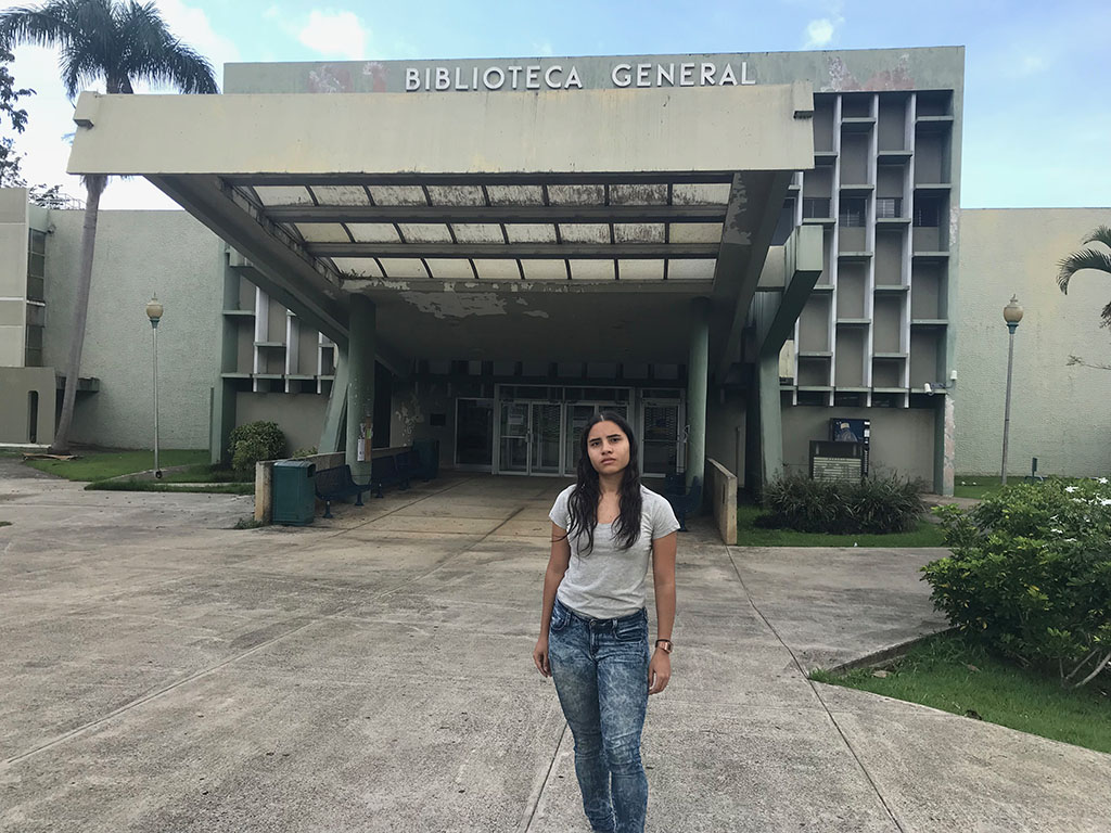 Daniela Perez in front of shuttered library in Puerto Rico A young woman stands in front of a gray building.