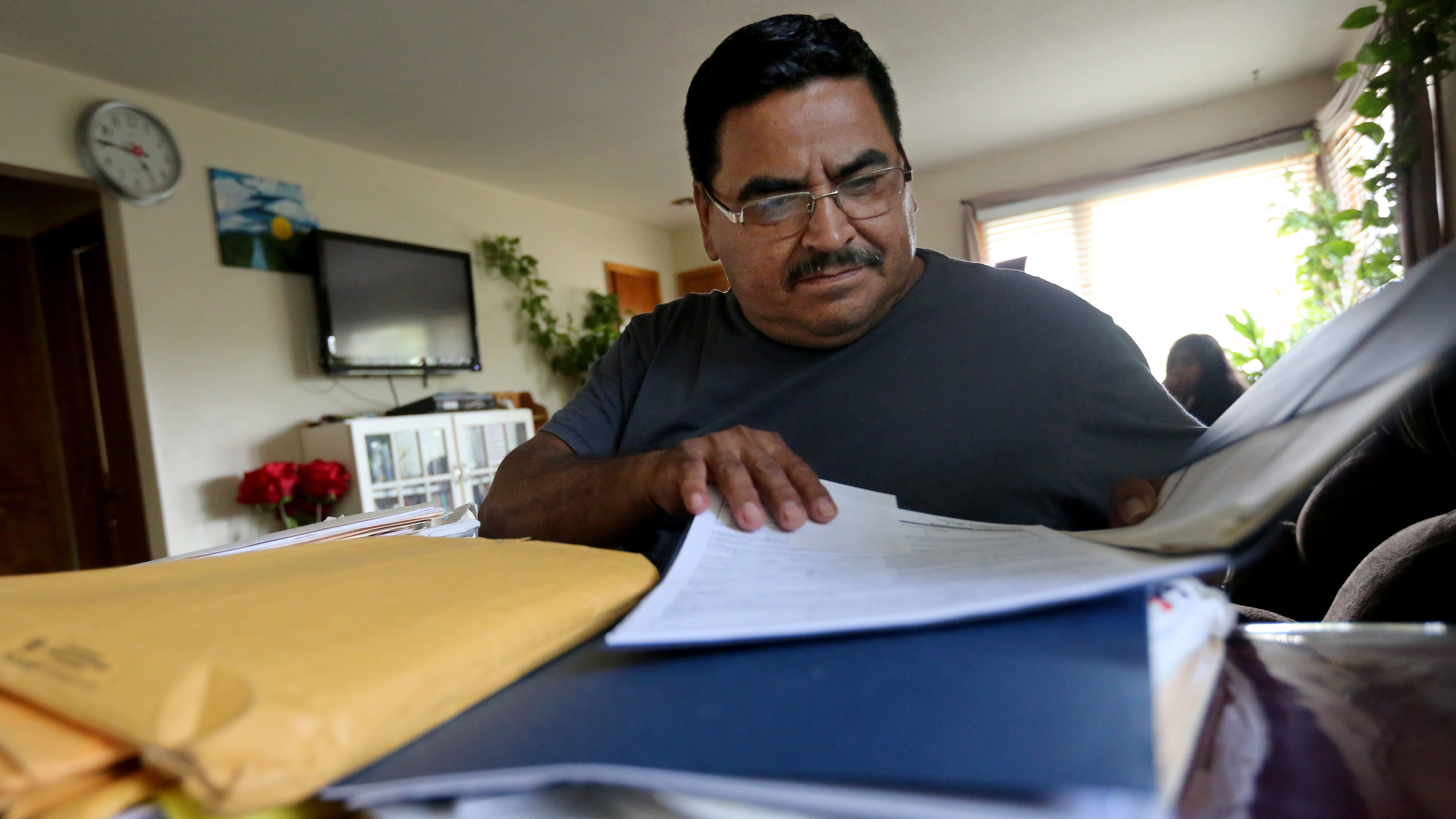 Man sits behind large stack of papers, brown envelopes