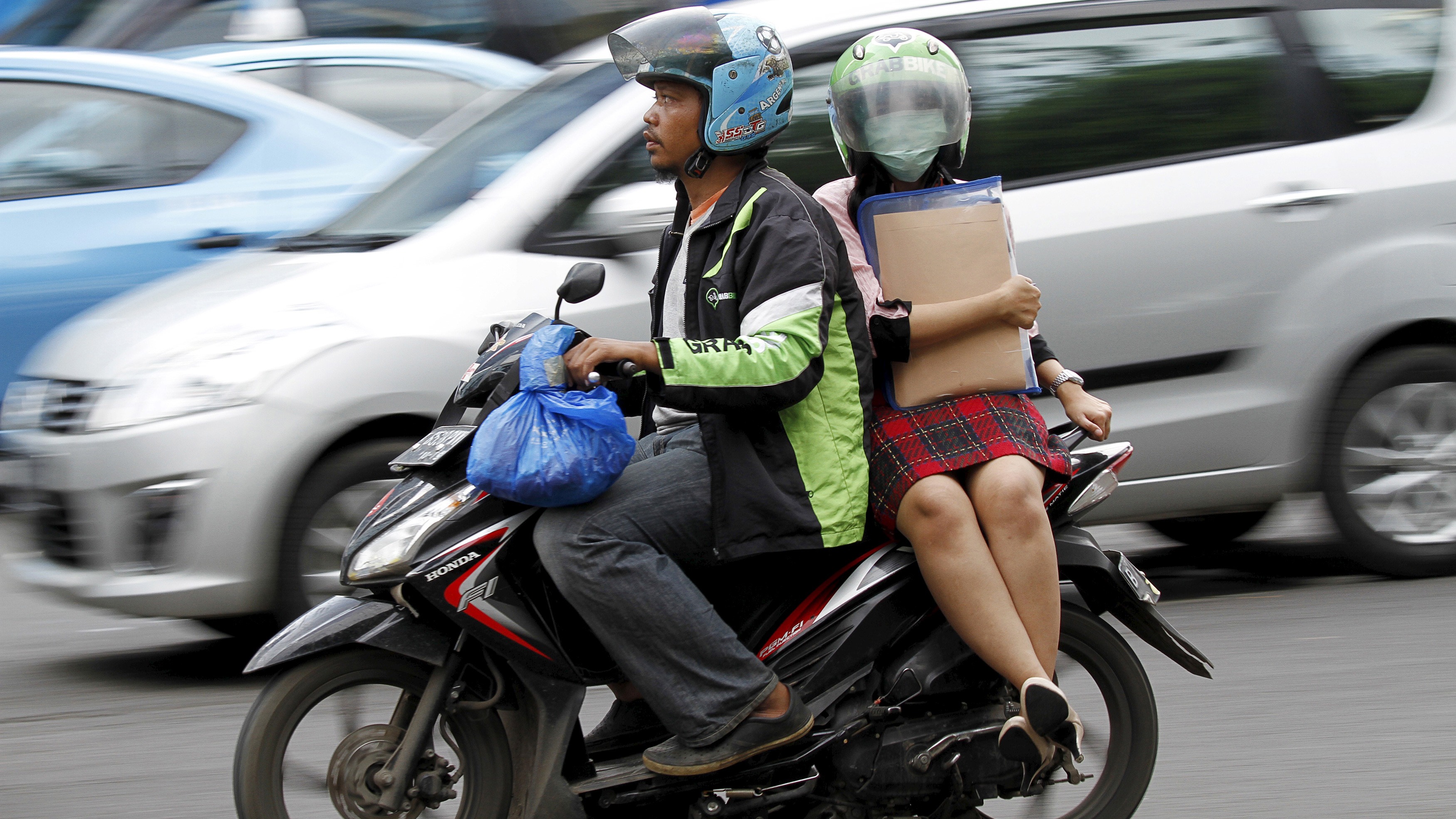 A woman rides on the back of a motorbike, part of the GrabBike ride-hailing service, on a busy street in central Jakarta, Indonesia 