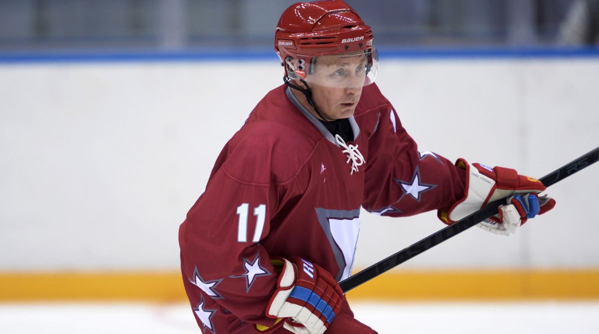 Vladimir Putin plays hockey. Vladimir Putin holds a hockey stick dressing in a red and white hockey uniform and helmet.