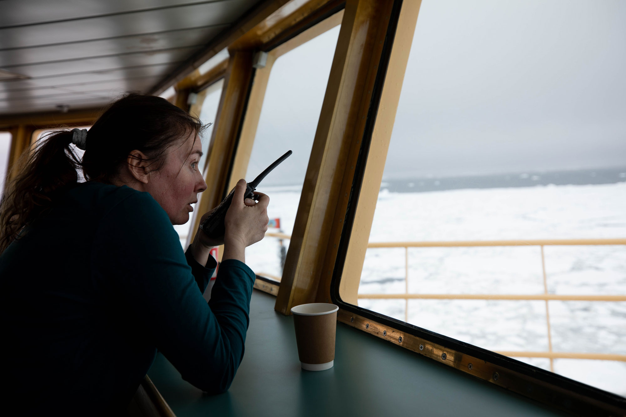 University of Gothenburg oceanographer Anna Wåhlin, director of the Hugin project, waits on the bridge of the Nathaniel B. Palmer for the Hugin submarine to surface in icy seas near the face of Thwaites Glacier. Researcher Anna Wåhlin is shown with a microphone looking out on the ocean.