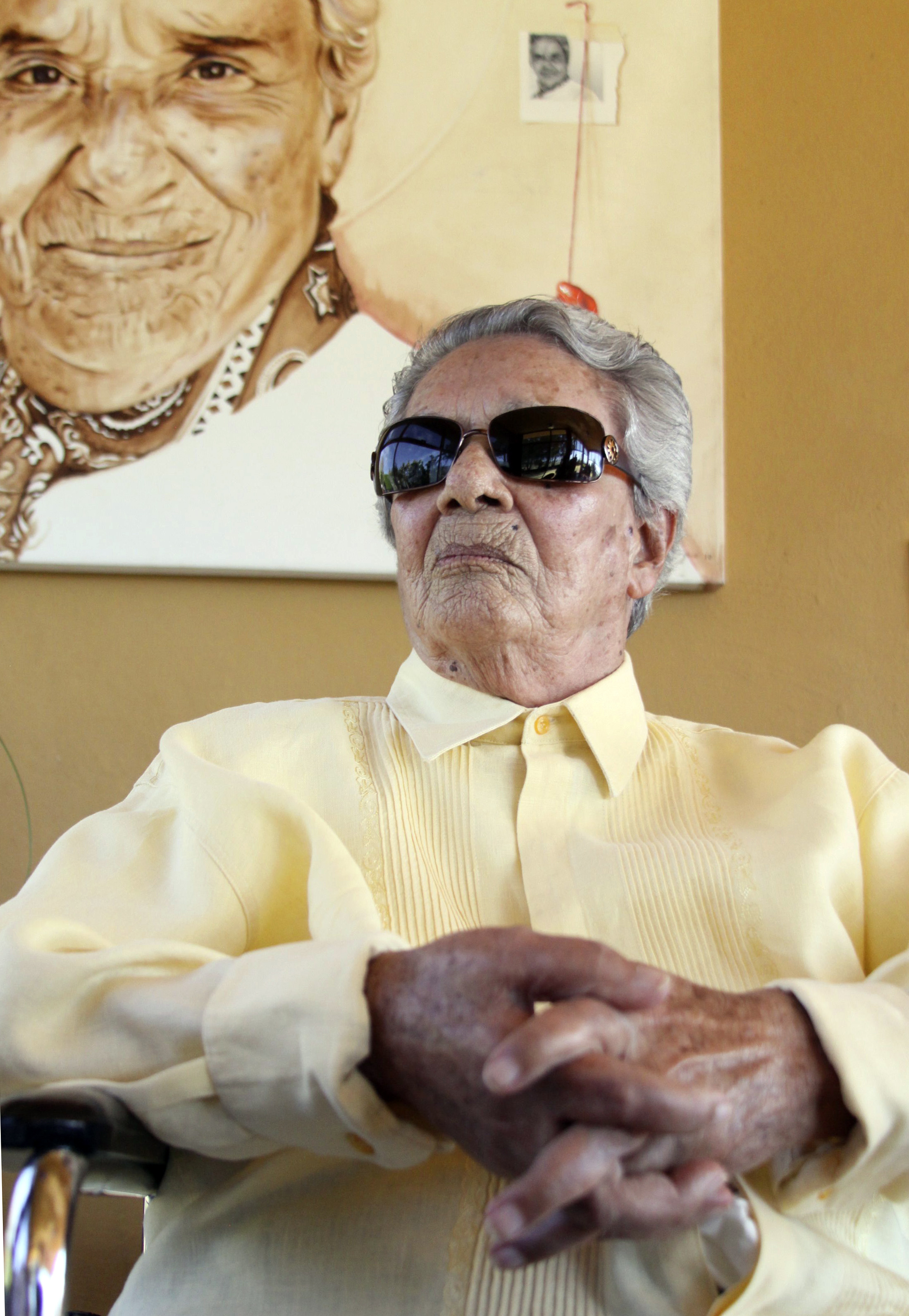 Legendary Costa Rican singer Chavela Vargas sits underneath a portrait of herself at her home in Tepoztlan, Feb. 2, 2011. Chavela Vargas wears a yellow blouse and sunglasses and sits in front of a her painted portrait.