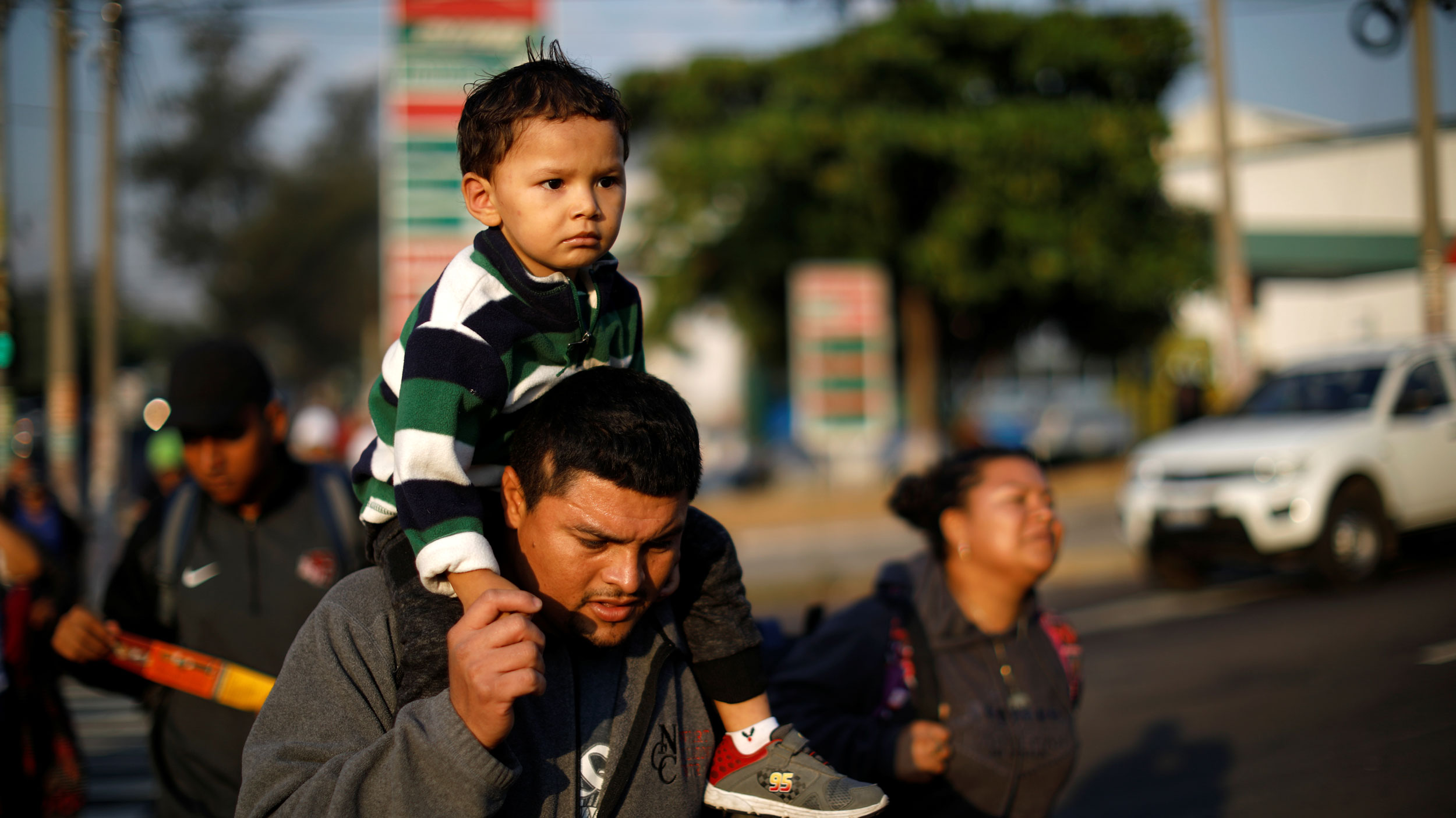 A father and son walk in a caravan of migrants departing from El Salvador en route to the United States, March 30, 2019. A father is shown holding his son on his sholders as they walk in a caravan of migrants en route to the United States.