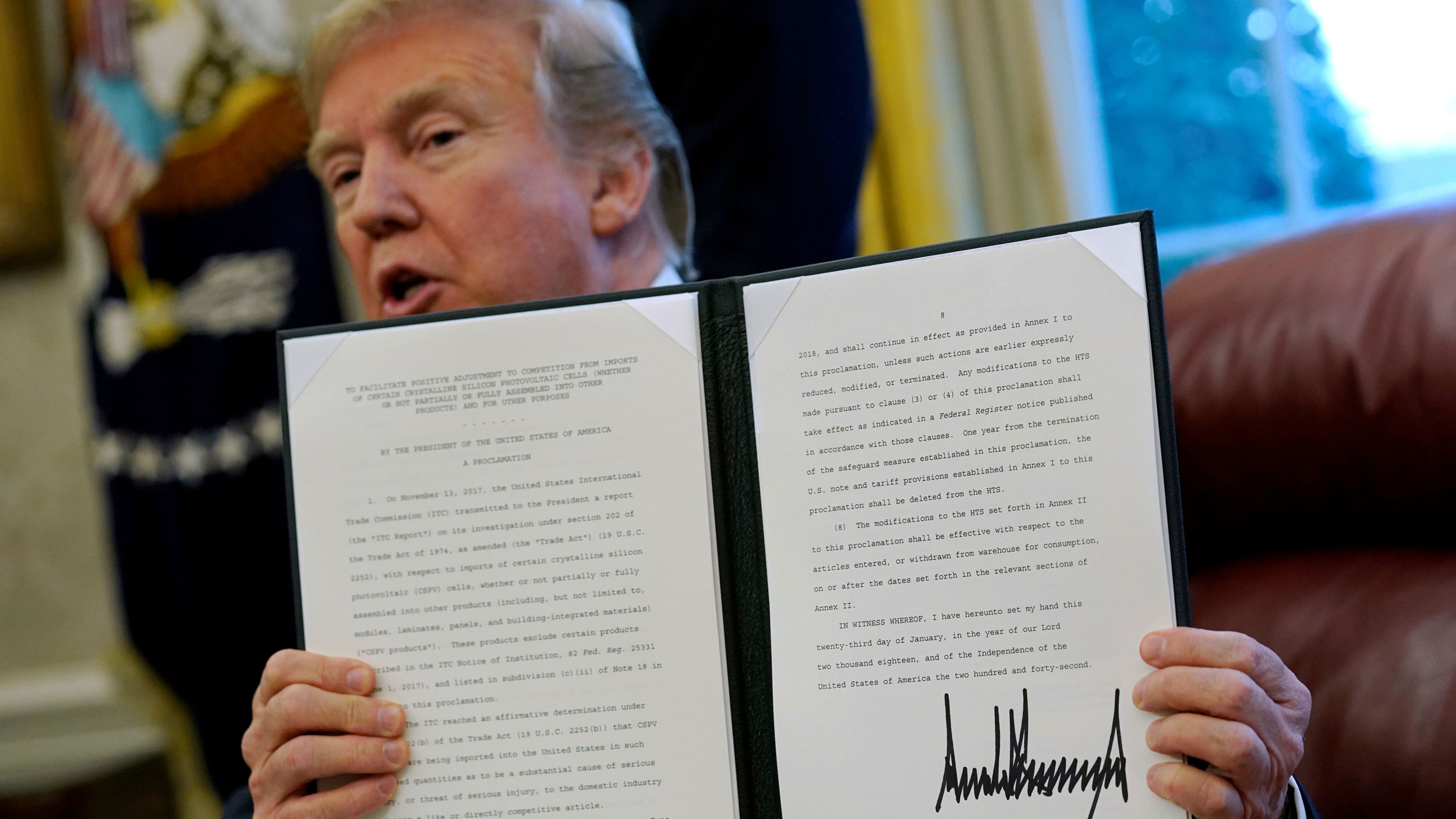 US President Donald Trump speaks to reporters after signing directives to impose tariffs on imported washing machines and solar panels. Donald Trump is shown holding.a folder with a directive typed out and his signature.