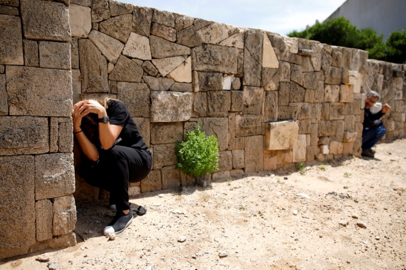 Two people cover their heads next to a wall.