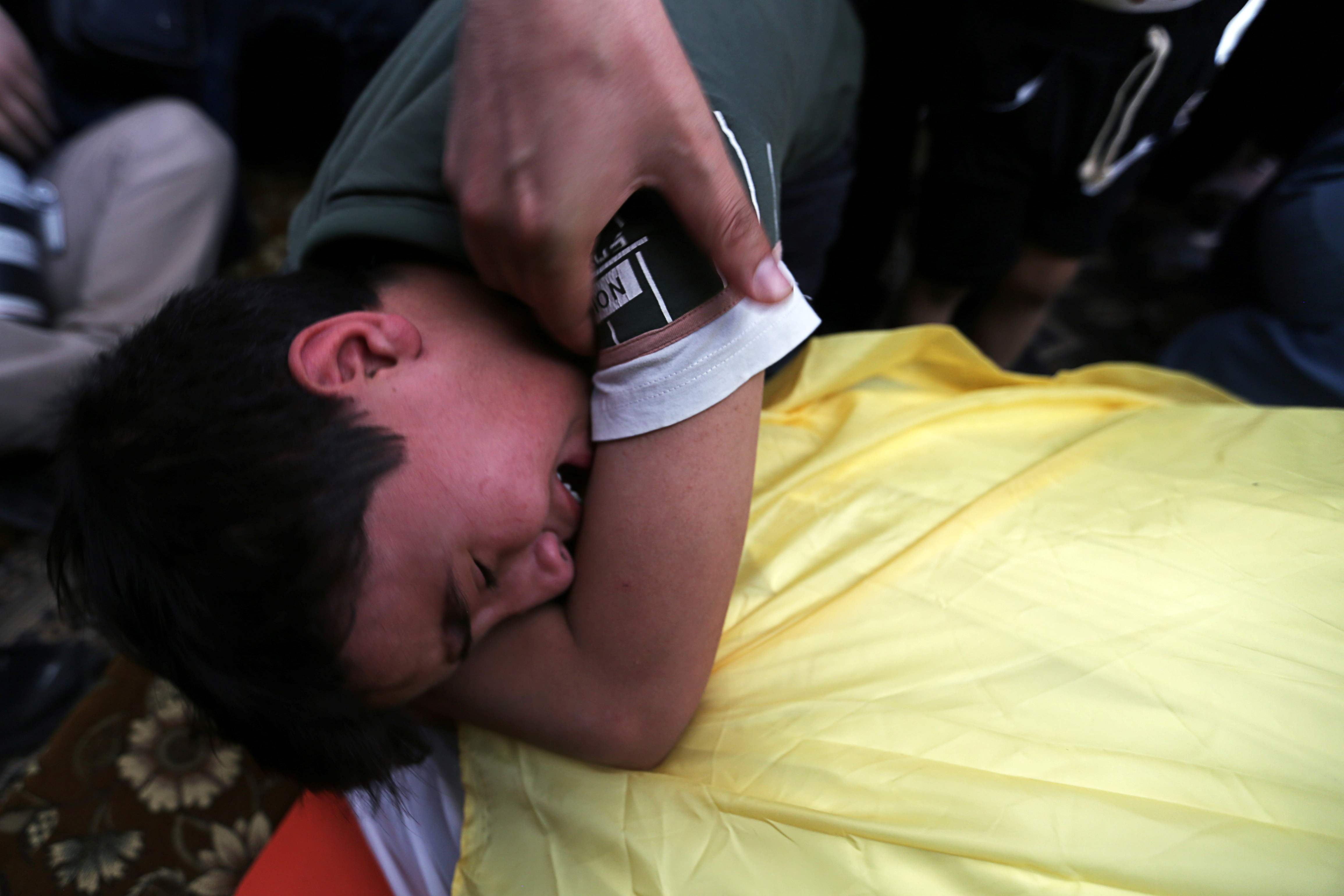 A boy sobs over the covered body of his father A boy sobs over the covered body of his father as a hand holds the boys shoulder.