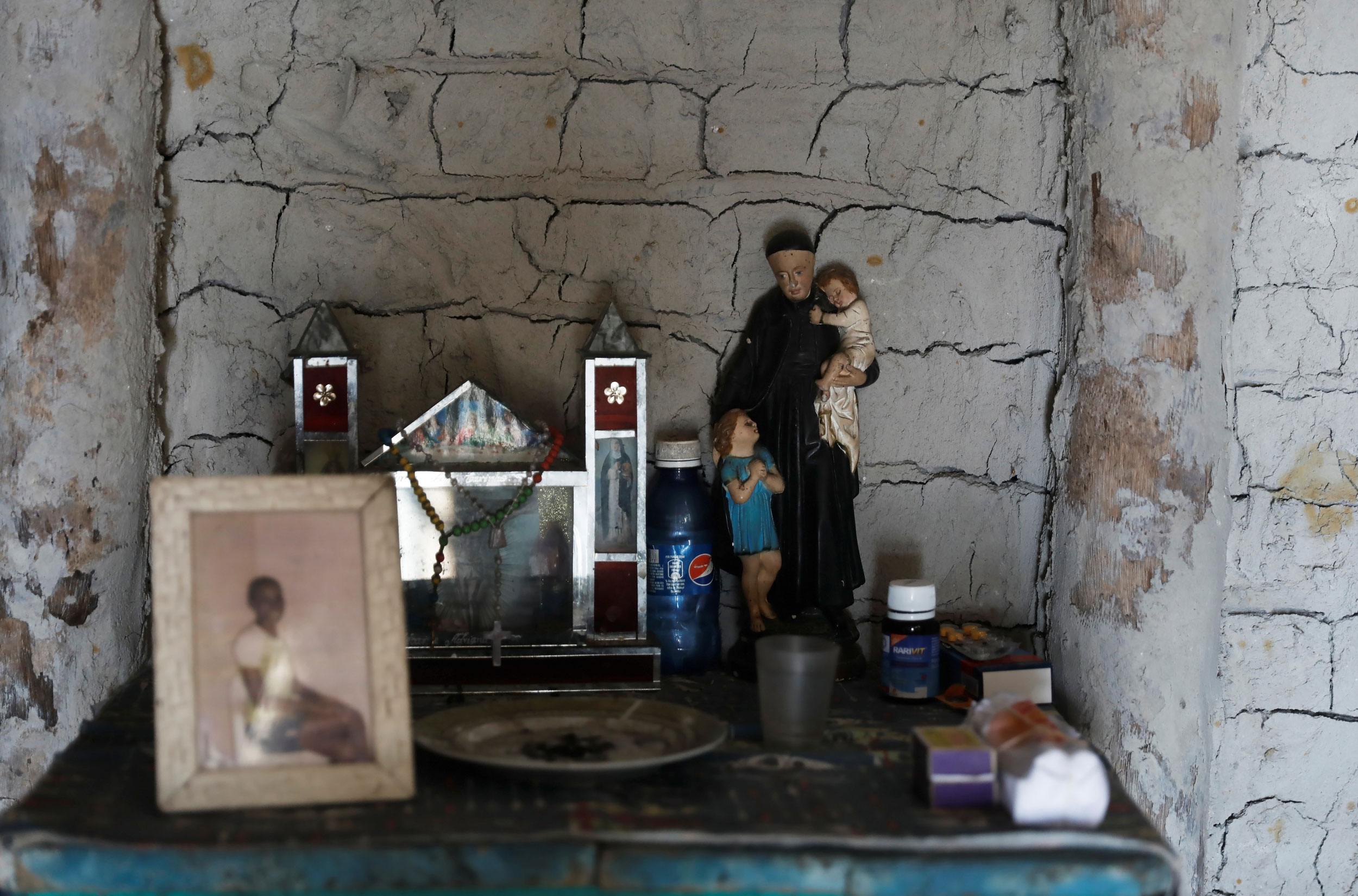 A shrine is seen inside the house of fisherman Jose da Cruz and his wife Vandeka. A shrine is seen with a framed photograph, a bottle of Pepsi and other items on a shelf.