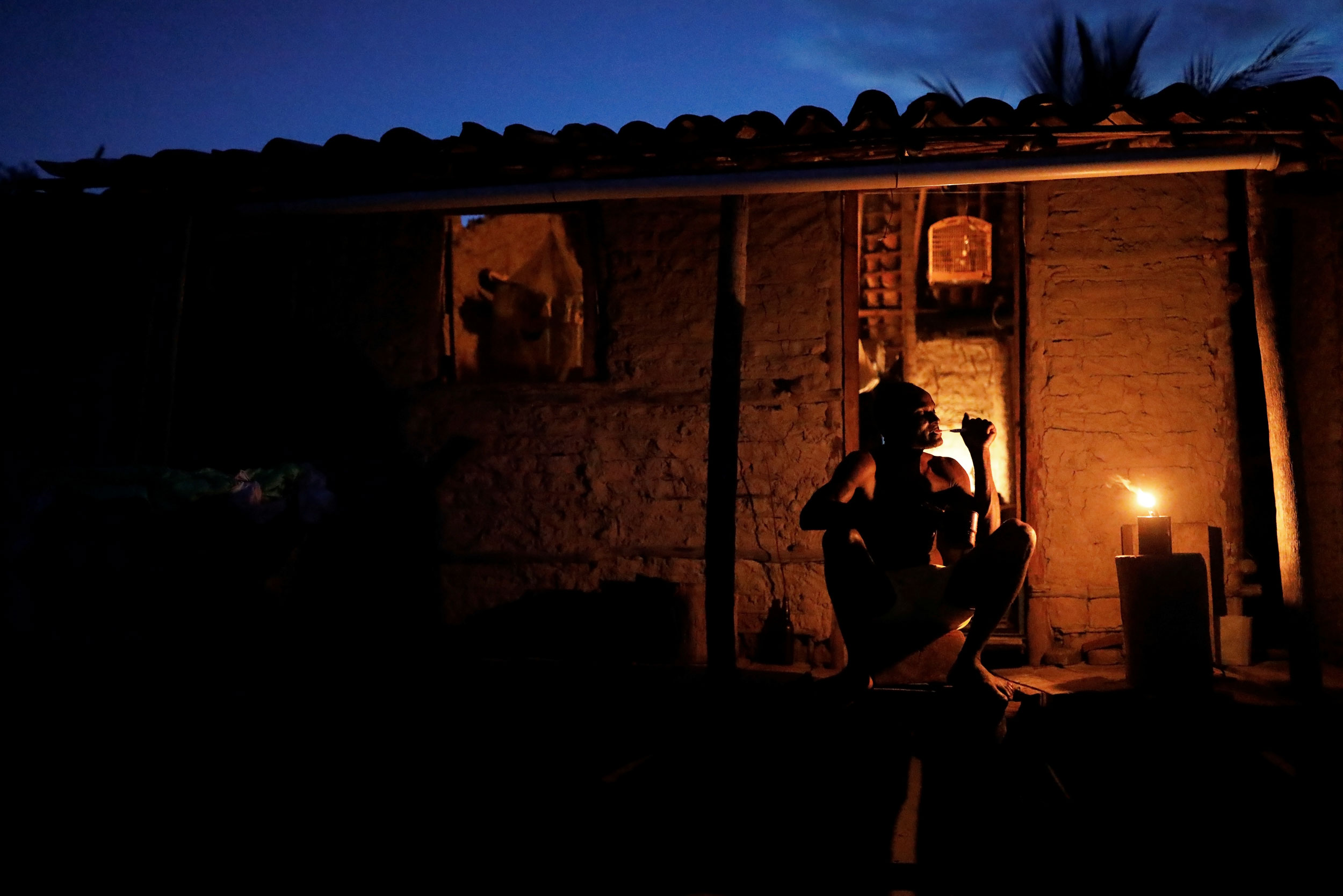 Cruz brushes his teeth. A man is shown sitting and brushing his teeth in a dark photograph at night with only the light from the house glowing.