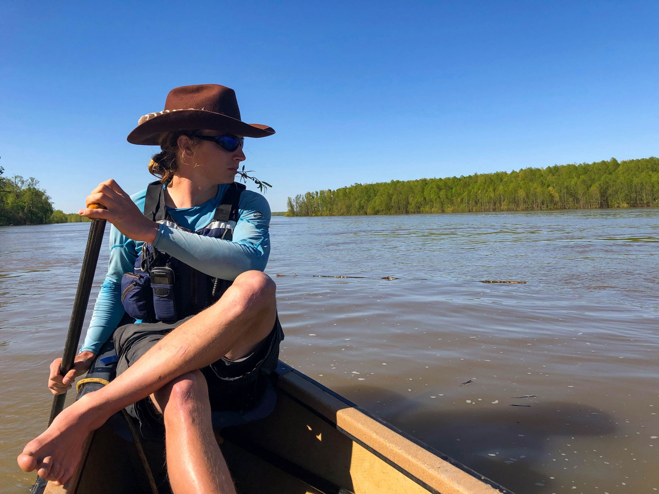 Canoe guide Tanner Aljets with the Quapaw River Company paddles through an area of Helena, Arkansas A man is shown in the back of a canoe with a paddle in his hand while wearing a wide-brimmed hat.