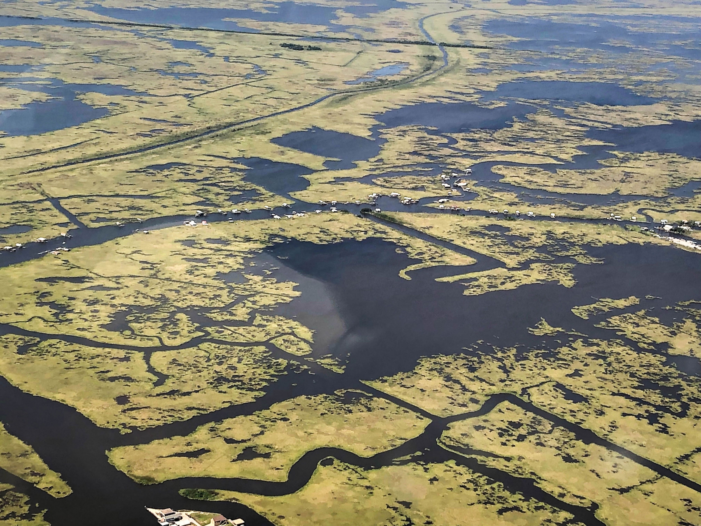 Communities and houses cling to vanishing land in the Mississippi River Delta south of New Orleans. Several houses are shown from above in an airplane with very little land for the houses to sit on.