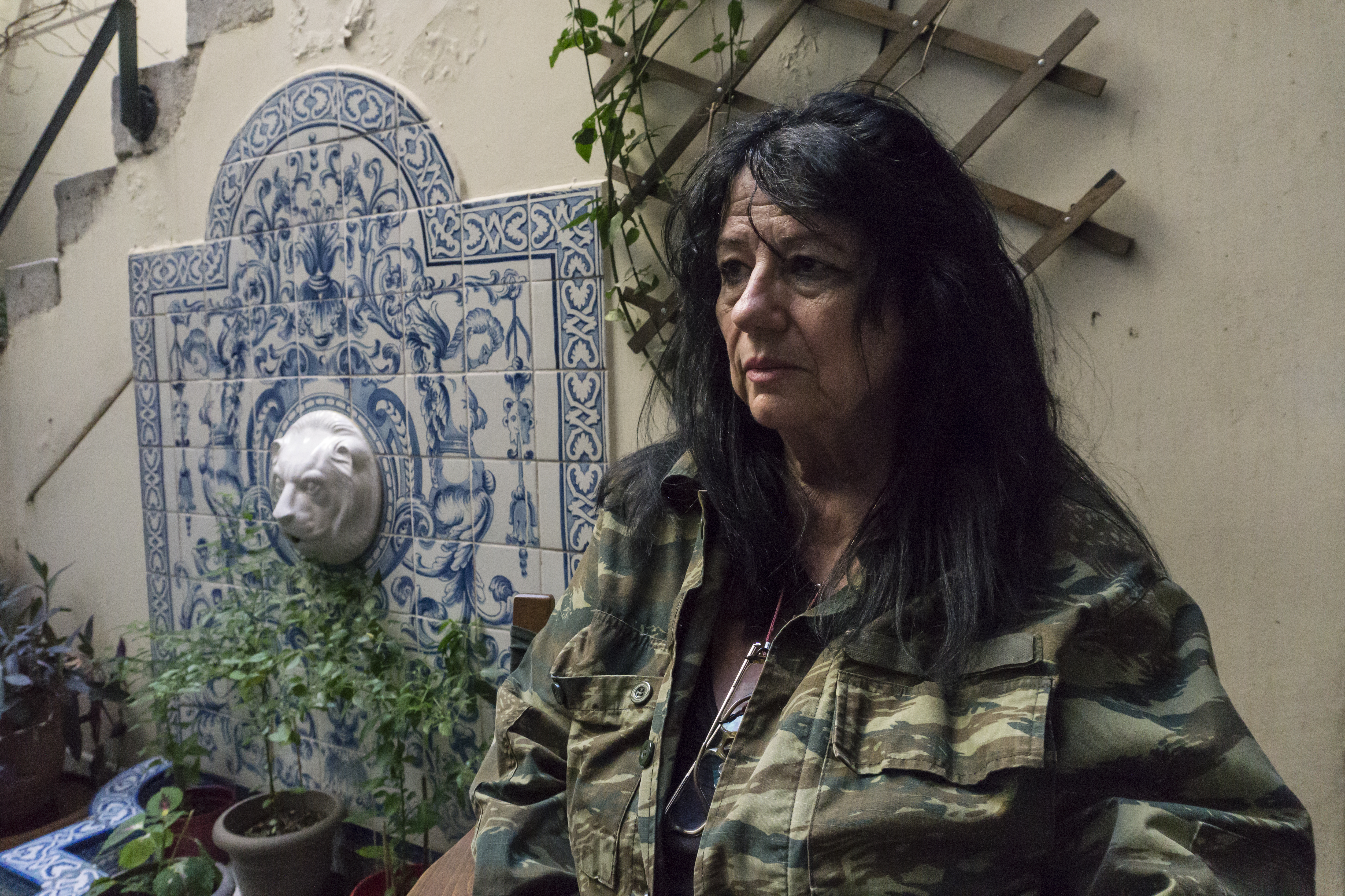 Anna Vagena, a member of the SYRIZA party, advocated for the right to build a private crematorium in Parliament and managed to change the law that opened the way for the crematorium at Ritsona. A woman with dark hair and army jacket stands near a tiled fountain