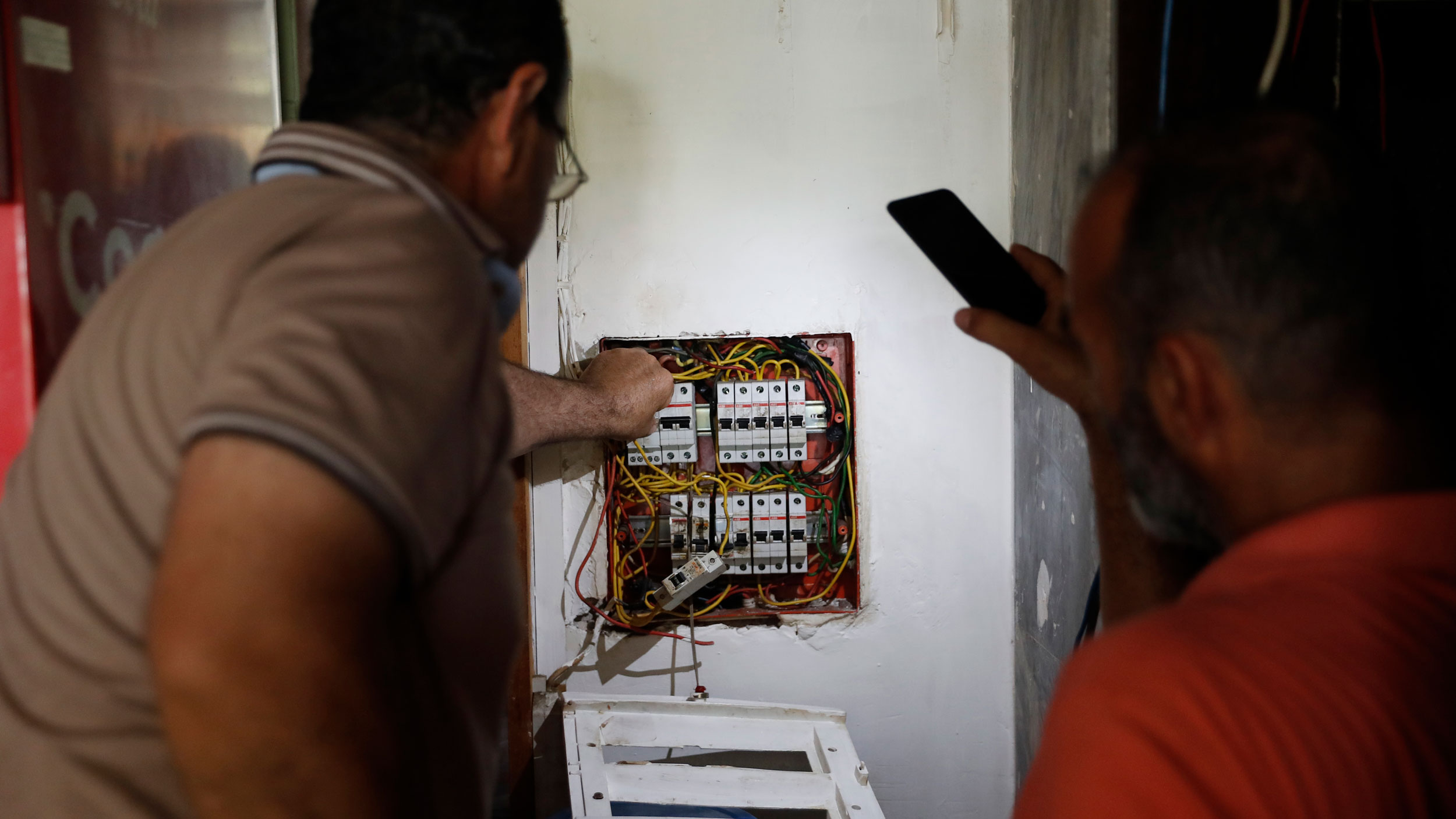 A Lebanese man, right, lights by his mobile phone for an electrician
