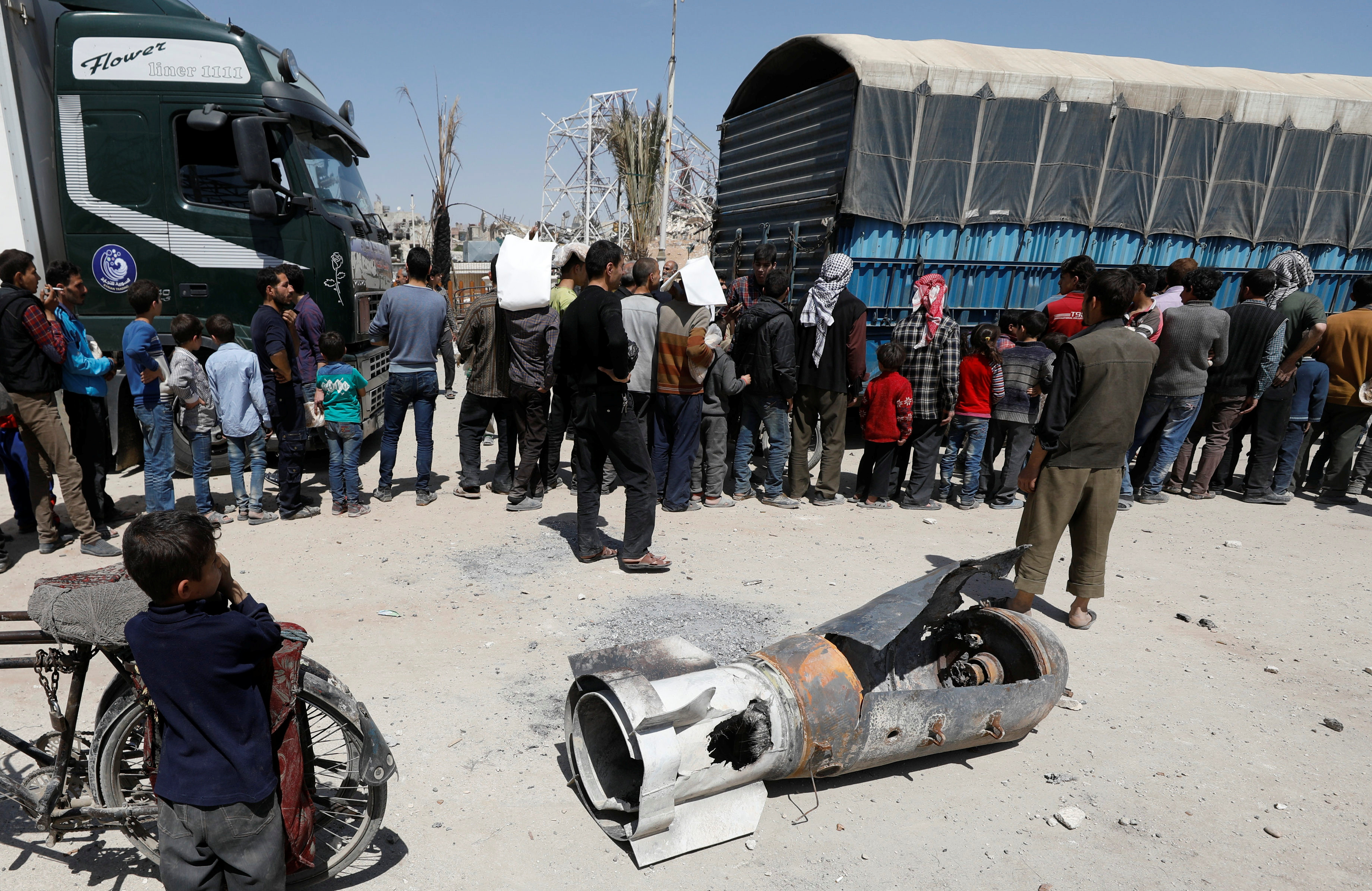 A boy stands next to the remains of a missile at the city of Douma in Damascus, Syria, April 16, 2018. A boy stands next to the remains of a missile as people line up for aid in the city of Douma in Damascus, Syria, on April 16, 2018.