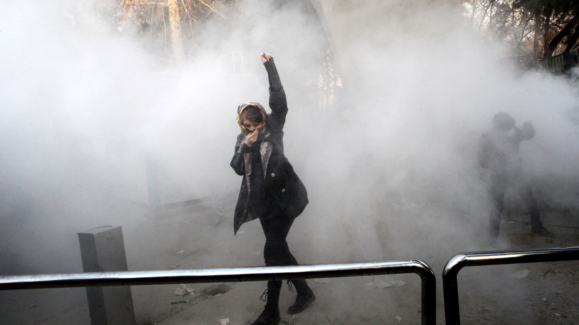 An Iranian woman raises her fist amid the smoke of tear gas at the University of Tehran during a protest, Dec. 30, 2017. An Iranian woman raises her fist, covering her face with a scarf, as smoke surrounds her.