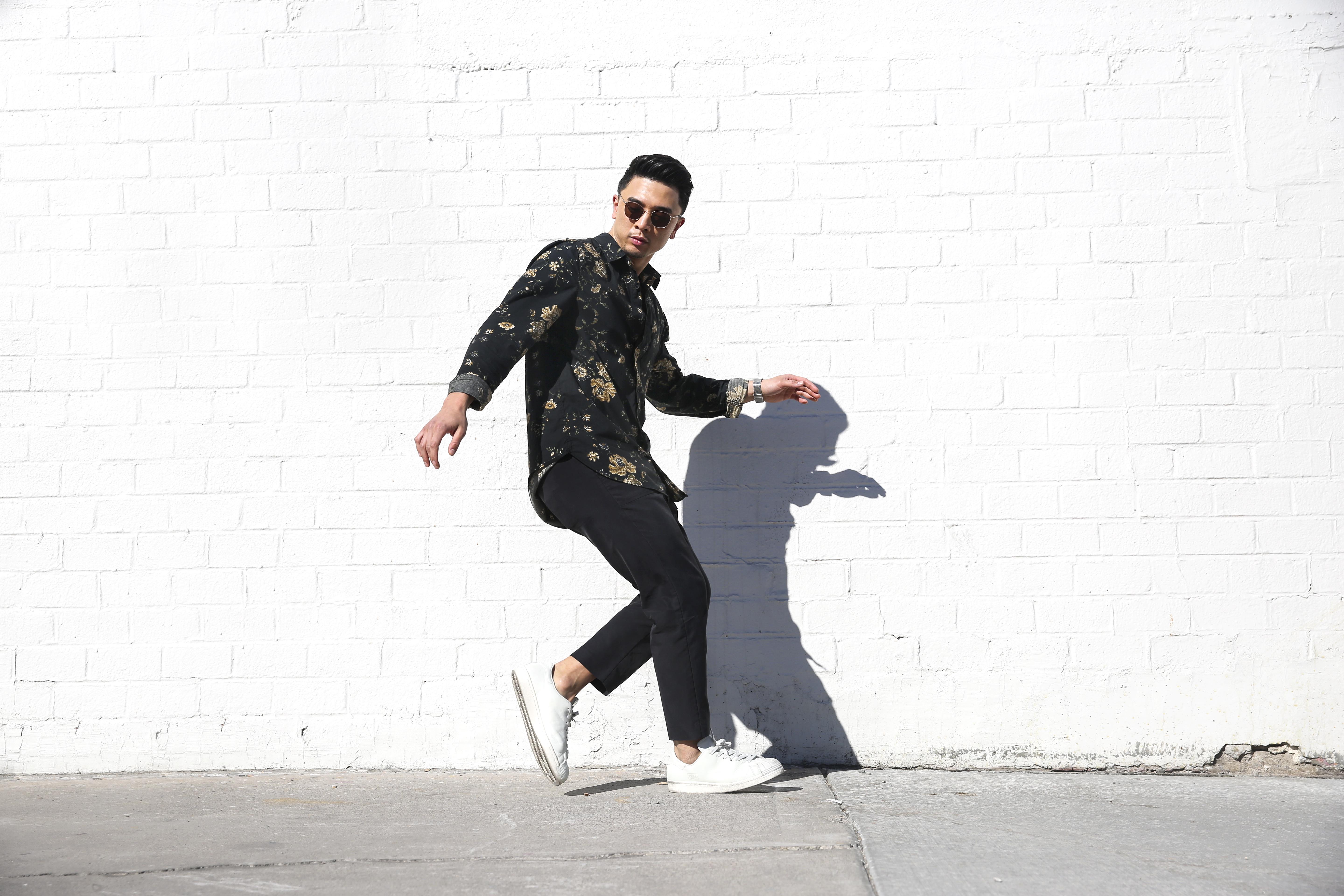 Man in sunglasses in dance pose in front of white, brick wall