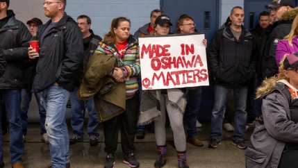 A GM worker in Canada holds a sign in red letters.