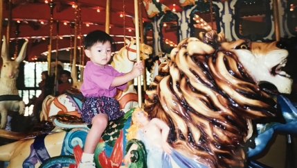 Boy on horse in carousel, looking at camera. Old, scanned photo
