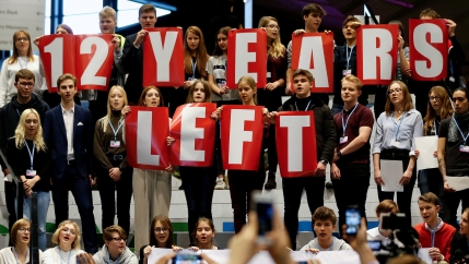 A group of school children hold signs that read