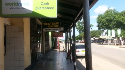 A strip of closed offices and empty sidewalk with a single woman waiting for offices to open. 