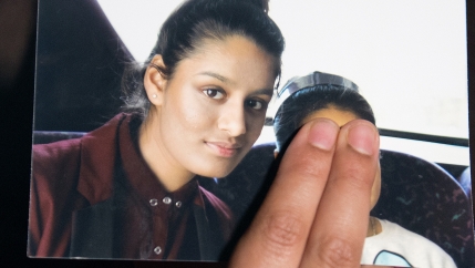 A girl holds a photo with her thumb over a face.