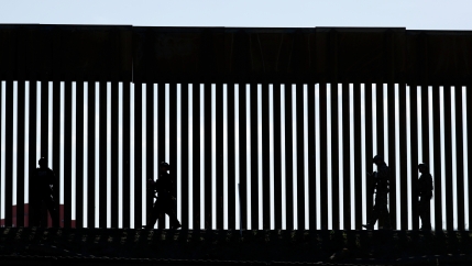 Shadow of patrolmen along slated wall at US border.