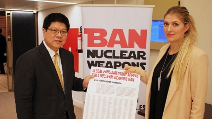 Two diplomats stand in front of a sign that reads ban nuclear weapons