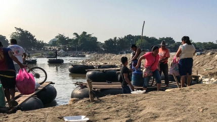 Several people are shown on the beach next to large floating rafts with wooden tops.