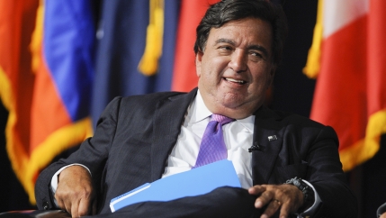 A man sits down with flags in the background