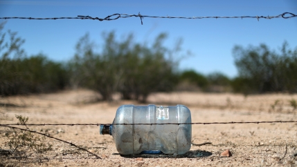 An empty water bottle lays on the dirt behind a string of barbed wire