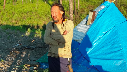 A man stands outside next to a tent.
