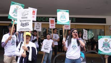 Protesters with signs stand in front of a Starbucks storefront.