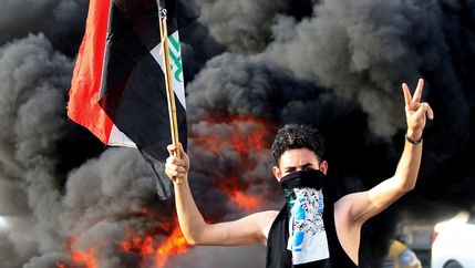 A demonstrator gestures as he stands close to burning tires blocking a road during a protest over unemployment, corruption and poor public services, in Baghdad, Iraq, on Oct. 2, 2019.
