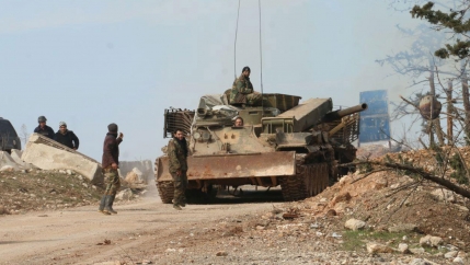 Several Syria soldiers are shown walking alongside and riding on a tank in a dirt road.