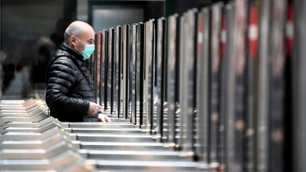 A man is shown walking through a gate to a train station while wearing a face mask.