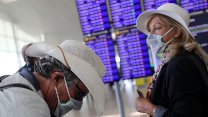 A man is shown hearing a white hat and looking down while wearing a face mask near a woman wearing a white hat and wearing a face mask.