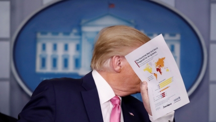 US President Donald Trump is shown hiolding a paper in his hand and covering his face.