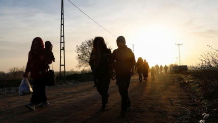 Several people are shown in shadow with the sun setting behind them and walking in a dirt road.