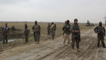 A group of soldiers are shown wearing fatigues and carrying weapons while standing in a dirt road.
