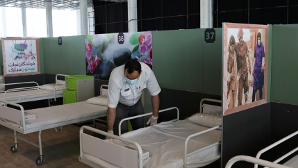 A man makes a bed in a row of beds with medical posters on the dividing walls 