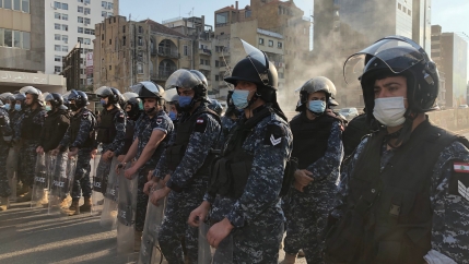 People in military uniform wear face masks while they form a line on a Beirut street during protest.