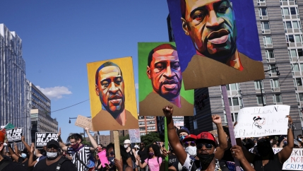 A large group of people are shown holding up signs with three people holding posters of George Floyd.