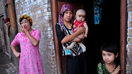 An ethnic Uighur woman hugs her son as she stands outside her house with her daughter and neighbors