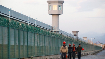 Workers in hard hats and construction vests walking by a fence.
