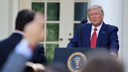 US President Donald Trump is shown standing at a podium and wearing a blue suit and red tie.
