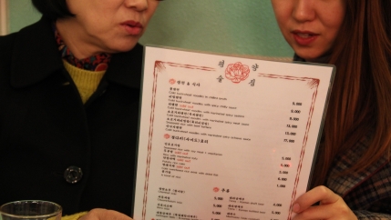 Han (left), a North Korean defector who asked that her full name not be used, and Kim Eun-joo (right) hold a menu together while examining the selection of North Korean dishes offered by the pub.