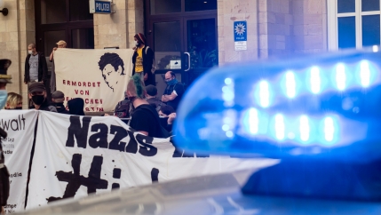 A sign with the written word nazi in black appears near the blue lights of a police vehicle 