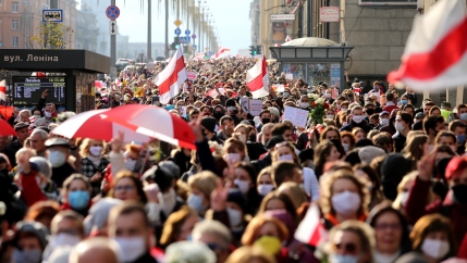 Mass of people wearing masks march with red and white umbrellas. 