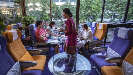 A flight attendant is serving meals in a flight-themed restaurant complete with airline seats and cabin crew to customers at Thai airways head office in Bangkok, Oct. 3, 2020. 